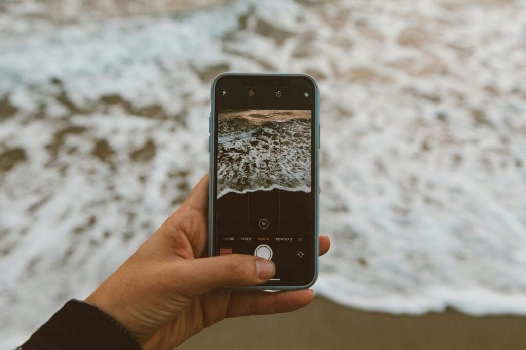 A hand holding a smartphone captures waves on a beach. Perfect for technology and travel themes.